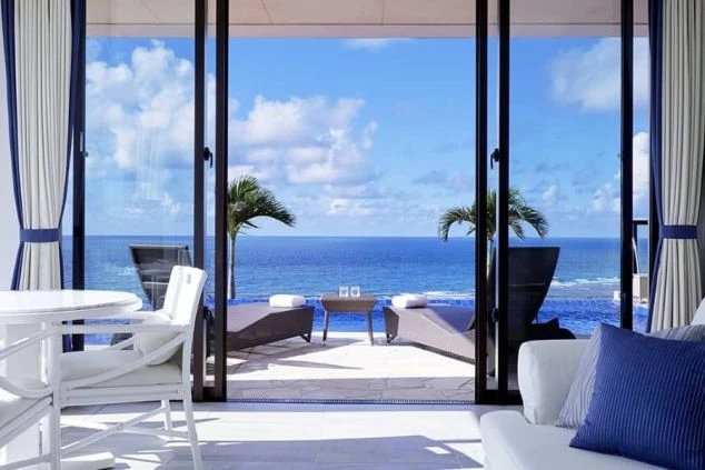 客室からプール越しに真っ青な海が見える、最高級リゾートホテルのテラスの画像。