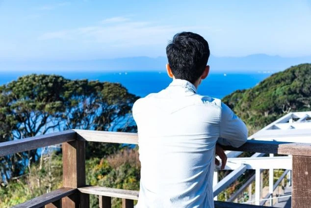 山々と海が広がる展望台で、男性が景色を眺めている後ろ姿の画像。青空と雄大な自然が広がるリゾート地の風景である。リゾートバイトの休日の過ごし方や観光を表す画像