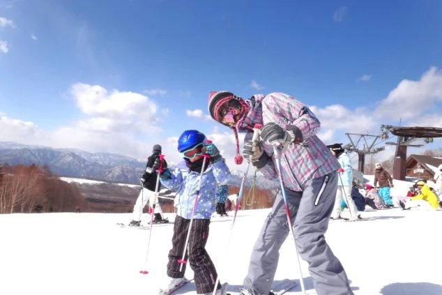 スキー場でスキーを楽しむ子どもと大人の画像。青い空と白い雪山を背景に、楽しそうに滑っている。リゾートバイトの休日にウィンタースポーツを満喫している様子。