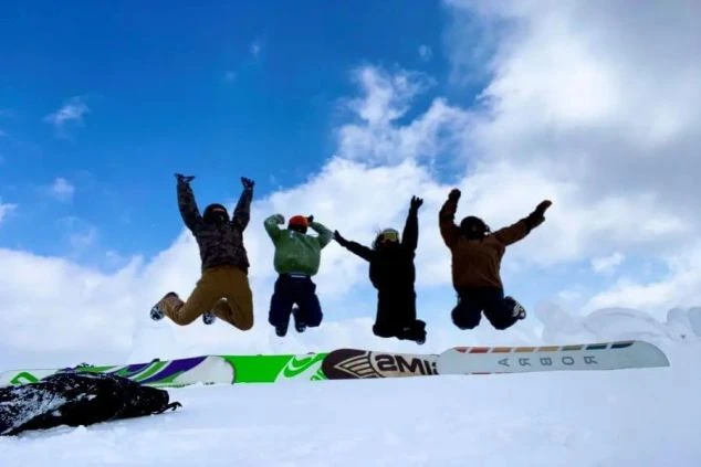 リゾートバイト仲間と雪山でジャンプする様子。冬のリゾート地で、仕事も遊びも全力で楽しむ非日常体験。