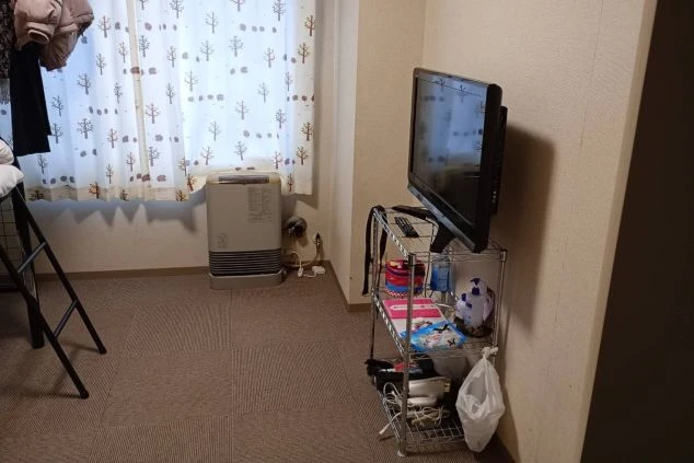 寮の居室にあるテレビと暖房器具。テレビの下には棚があり、生活用品が置かれている。