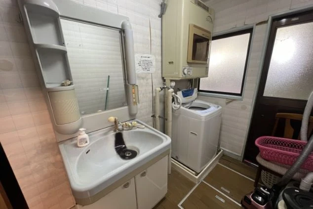 リゾートバイト女性寮の洗面所と洗濯機の画像。洗面台、洗濯機、乾燥機（または給湯器）が設置されており、生活に便利な設備が整っている。