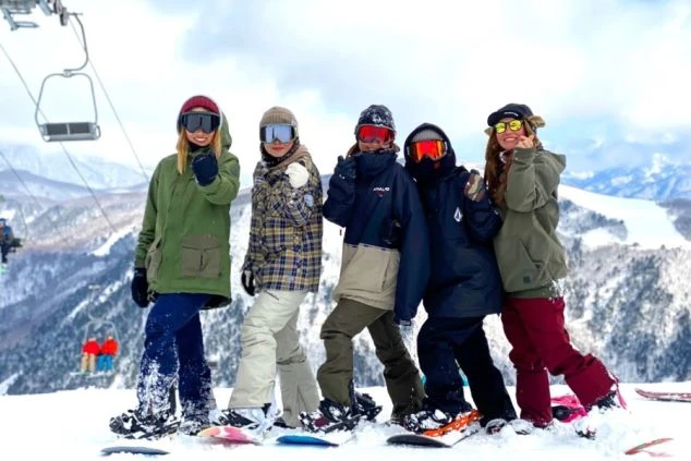 雪山でスノーボードウェアを着てポーズをとる友達グループ。リゾートバイトの休日にスキーや雪遊びを楽しむ若者。