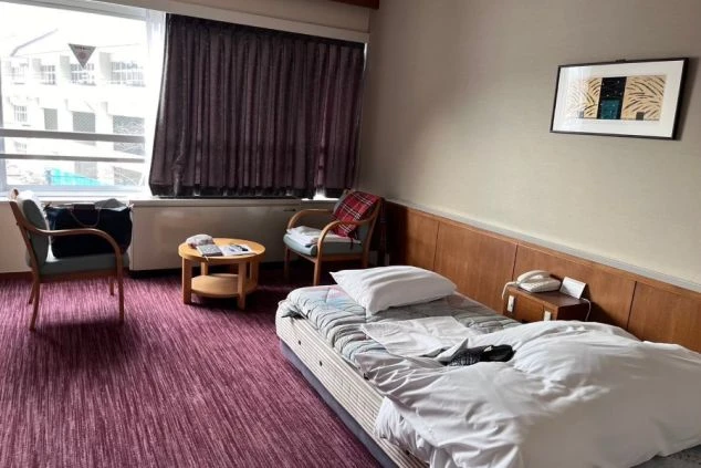 寮の和室。畳の部屋にローテーブル、座椅子、暖房器具、テレビが映る。