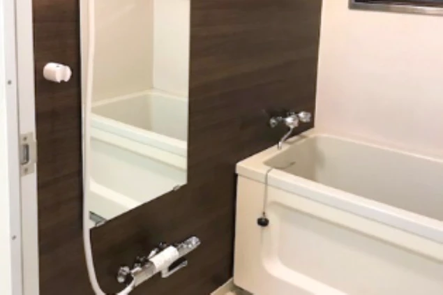 リゾートバイトの寮の浴室。白いバスタブが設置され、壁はダークブラウンの木目調パネルで清潔感のあるモダンな空間。