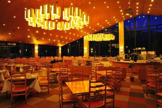 ホテルや旅館のレストラン。おしゃれな照明が灯り、多くのテーブルが並んでいます。