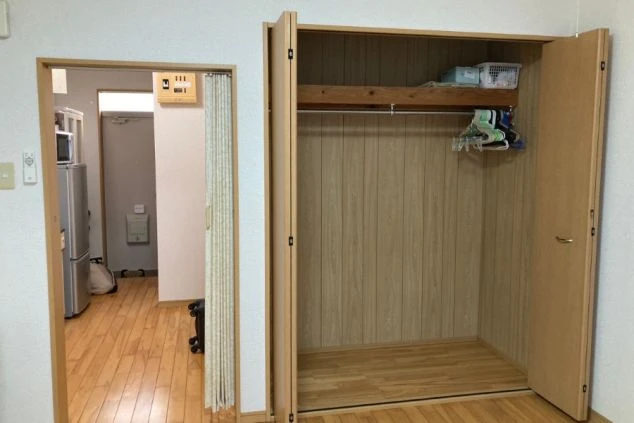 リゾートバイトの寮の収納スペースの画像。扉を開くと、ハンガーポールと棚があり、衣類や荷物を収納できる。