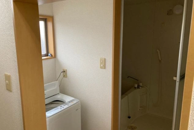 リゾートバイトの寮の洗濯スペースの画像。コンパクトなキッチンと洗濯機、奥には浴室が見える。