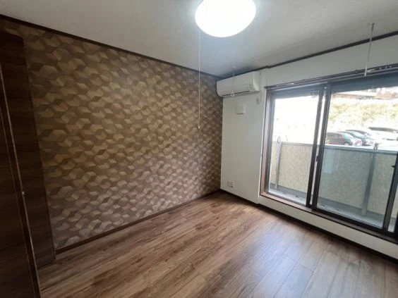 寮の個室。木目調の床と壁紙、エアコン、窓付きの部屋が映る。