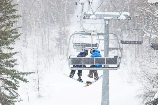 雪が激しく降る中、スキー場のリフトに乗る二人組のスノーボーダー。静かな雪山の雰囲気が伝わってきます。