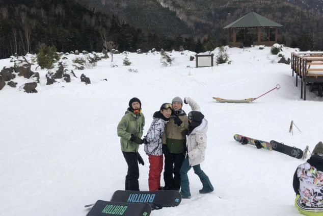 リゾートバイト仲間のゲレンデでの記念写真。ゲレンデに座り、雪山の景色を眺める冬の思い出作りの様子。