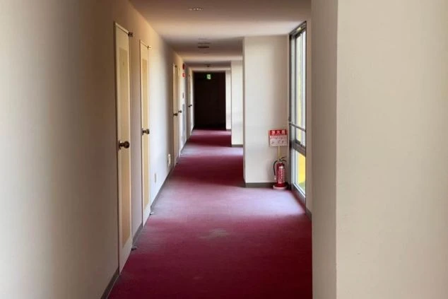 リゾートバイトの寮にある廊下。赤い絨毯が敷かれ、奥には個室のドアが並び、プライベートを確保している。