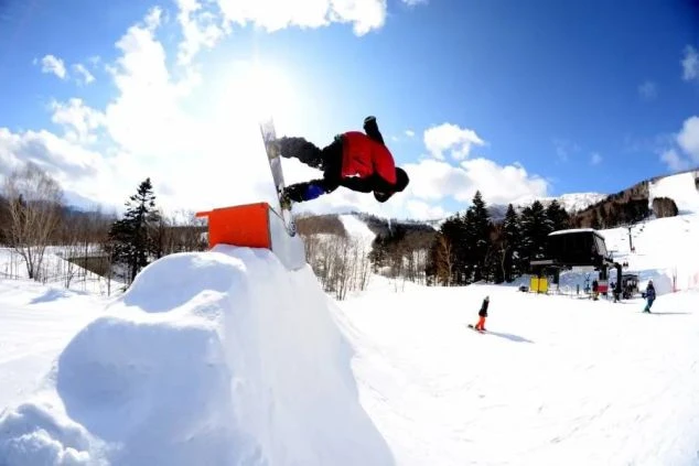 快晴のスキー場で、スノーボードでダイナミックなジャンプに挑戦。リゾートバイトの休日に、ウィンタースポーツを満喫できるイメージ。