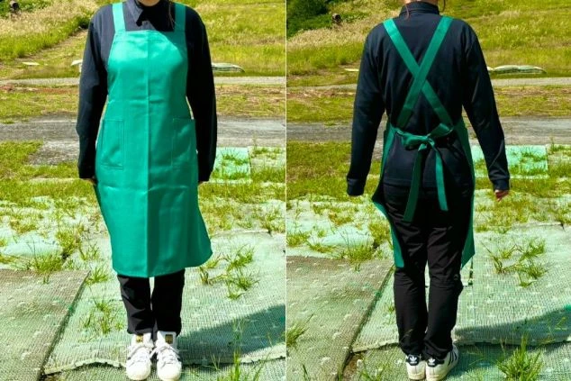 黒いシャツとパンツに、鮮やかな緑色のエプロンを合わせたスタイルです。