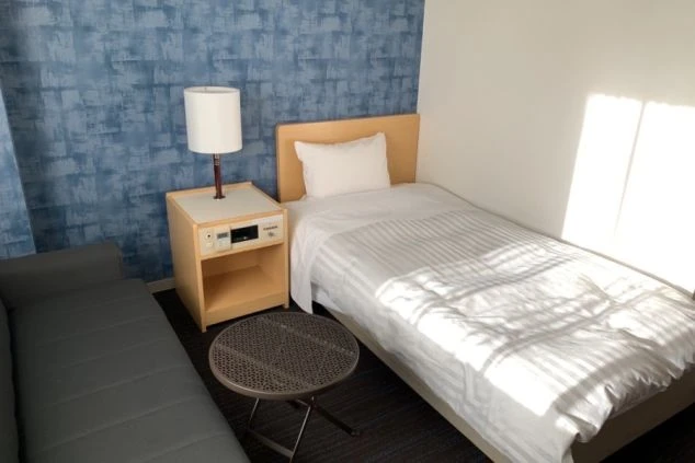 リゾートバイトの社員寮の部屋を表現するイメージ画像。青い壁紙の部屋にベッドとソファ、テーブルが備え付けられたシンプルな個室。