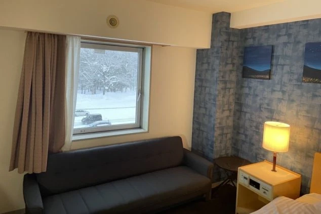 リゾートバイトの社員寮の部屋を表現するイメージ画像。窓から雪景色が見える、ベッドとソファがある洋室。