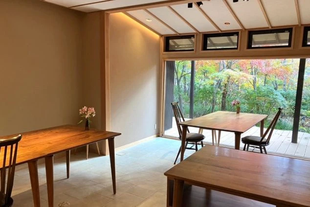 紅葉した木々が美しい庭に面した、木の温もりあふれるモダンな食事処の画像。