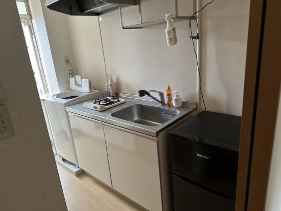 リゾートバイトの寮の共用キッチン。ガスコンロ、シンク、冷蔵庫、洗濯機が設置されており、自炊や生活に便利な設備の画像。