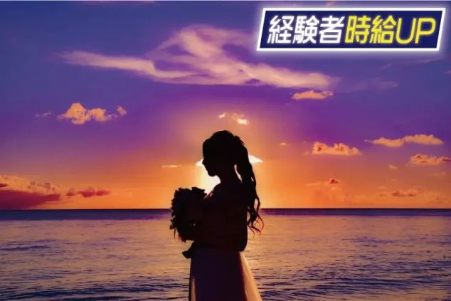 夕焼けの海辺で、花束を持った女性のシルエット。空は紫とオレンジ色に染まり、ロマンチックな雰囲気。画像の上部には「経験者時給UP」という文字が重ねられている。