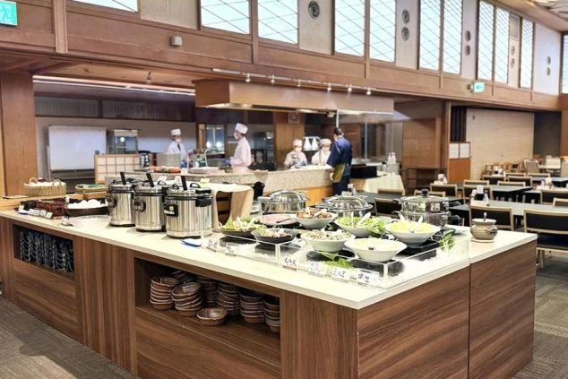 和の雰囲気漂う広々としたダイニング。丁寧に盛り付けられた料理が並ぶビュッフェ台と、奥のオープンキッチンで腕を振るう料理人たち。ワクトリで見つかるリゾートバイトの職場です。