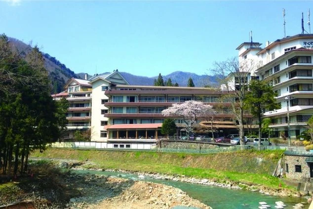澄んだ川のせせらぎと緑の山々を背に建つ立派な温泉旅館。エントランス付近には淡いピンクの桜が咲く、風情あふれる温泉地でのリゾートバイトをワクトリがご案内します。