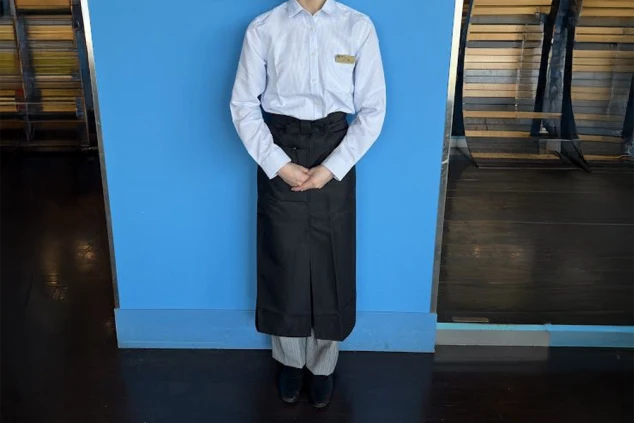 白いシャツに黒いエプロンを着用。カジュアルな雰囲気で、レストランサービスやホール業務の仕事をアピール。