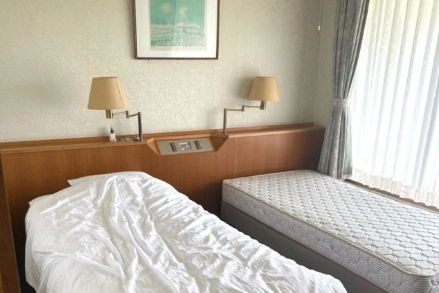 寮の個室。ベッドが2台並び、ランプと絵画が映る部屋の様子。