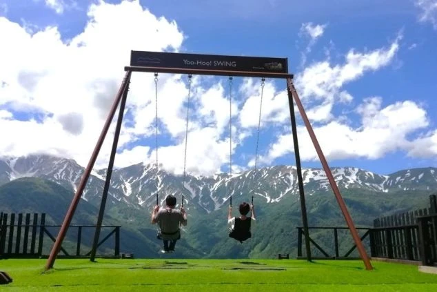 白馬岩岳マウンテンリゾートなどの展望エリアにある、雪山に向かって漕ぐブランコ（Yoo-Hoo! SWING）に乗る二人。リゾートバイト「ワクトリ」で絶景を楽しめる白馬の仕事。