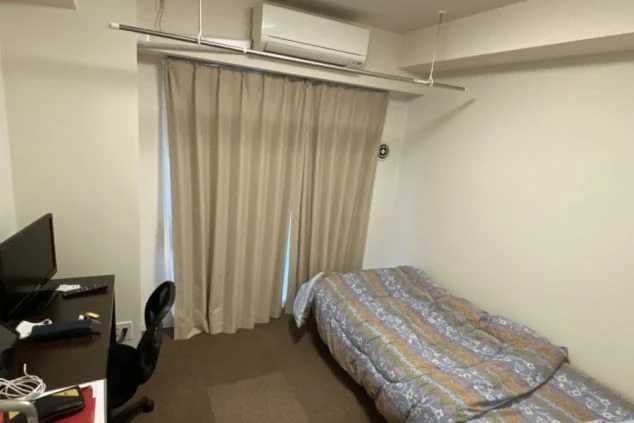 寮の個室。シンプルなシングルベッドと、テレビ・リモコン・小物が置かれたデスク、ワークチェアが備え付けられています。