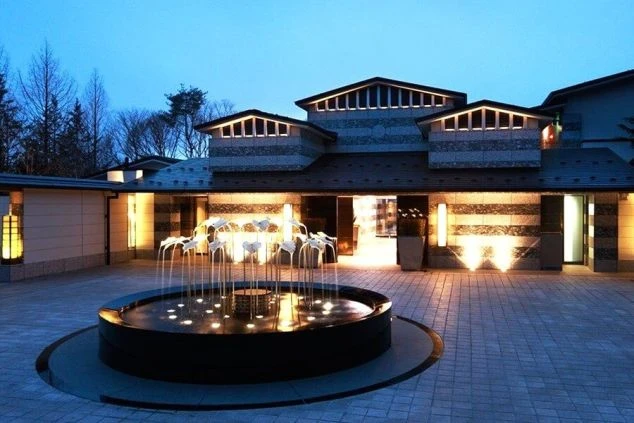 長野県軽井沢のホテルの外観の画像。夕暮れ時の深い青い空に、館内のオレンジ色の照明が映えている