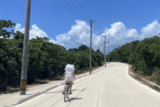 沖縄県竹富島の道を自転車で走っている画像。白い道路と青い空が印象的。