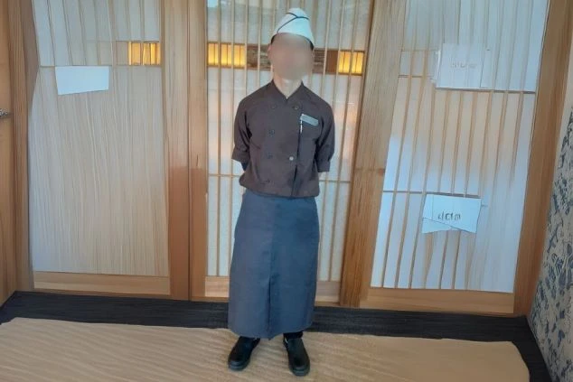 茶色の上着に紺色のエプロン、コック帽と黒いコックシューズを着用した、和食レストランの調理スタッフの制服。リゾートバイトで調理業務に興味がある方に、仕事内容と安全に配慮した服装のイメージを伝える画像。