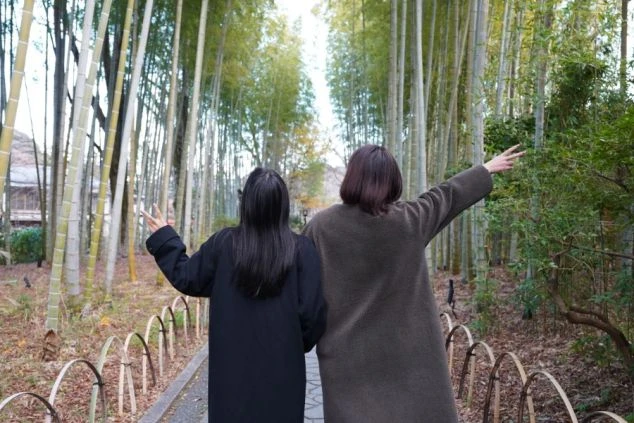 伊豆・修善寺温泉の観光名所「竹林の小径」で、寄り添ってピースサインを送る2人の女性ワクトリスタッフの後ろ姿の画像。