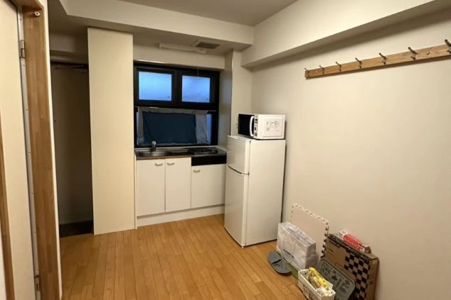 清潔なフローリングのキッチン・リビングスペース。冷蔵庫や電子レンジなどの家電が完備され、自炊も可能な広々とした居住環境。