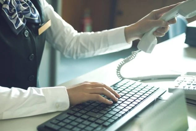 PCのキーボードを打ちながら受話器を取る女性の手元の画像。予約事務スタッフの仕事のイメージ。