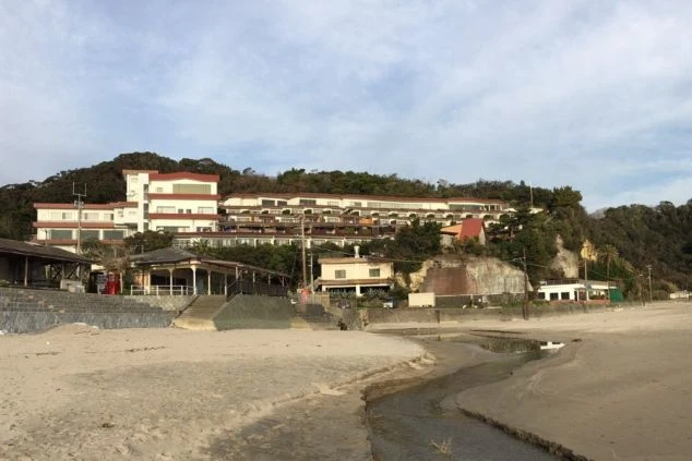 白い建物が階段状に広がり、手前には砂浜と、小さな川が流れる様子が見える。