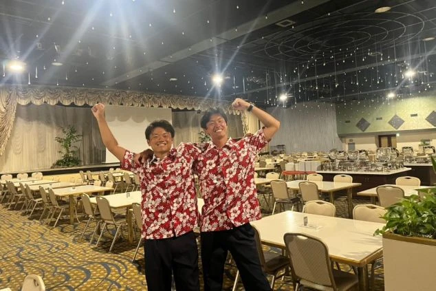 ワクトリでリゾートバイトをするスタッフが撮影した、静岡県伊豆のホテルのレストラン会場で、肩を組んでピースをしている2人の男性スタッフの画像。制服のアロハシャツを着ている。