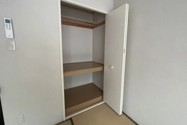 扉を開けると、ハンガーをかけるバーと、2つの棚が見える。たくさんの荷物が収納できる、寮の収納スペースの画像。