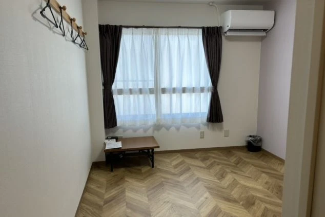 リゾートバイトの寮の部屋の中を撮影した画像。部屋にはフローリングの床と大きな窓があり、折りたたみ式のテーブルが置かれている。