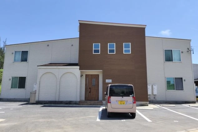 個室寮の外観の写真。建物の前には車が止まっている。