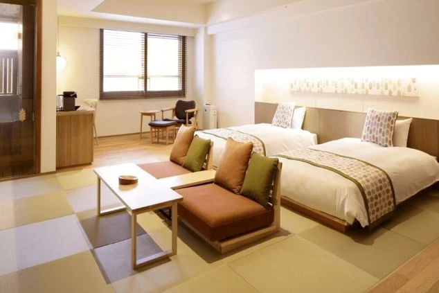 モダンな和室の客室。畳のスペースに二つのローソファとローテーブルがあり、フローリングのスペースに二つのベッドがある。