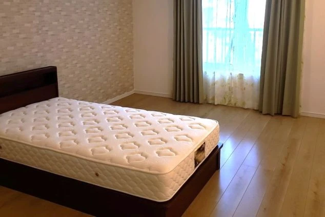 木目調のフローリングの部屋に、白いシーツが敷かれたシングルベッドとグリーンのカーテンがある。