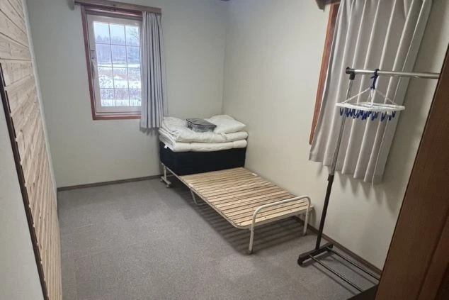 雪景色が見える窓があるリゾートバイトの個室寮。ベッドとハンガーラックが用意された、清潔感のあるシンプルな一人部屋。