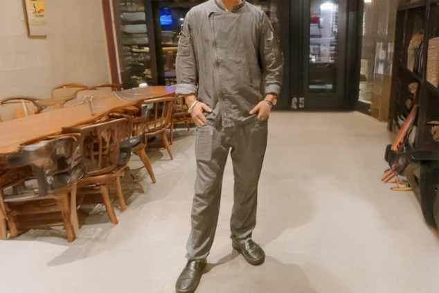 リゾートホテルの調理場で働く男性。グレーのコックコートとパンツを着用し、仕事に真剣に取り組む姿を連想させる。調理・調理補助のリゾートバイトをアピール。