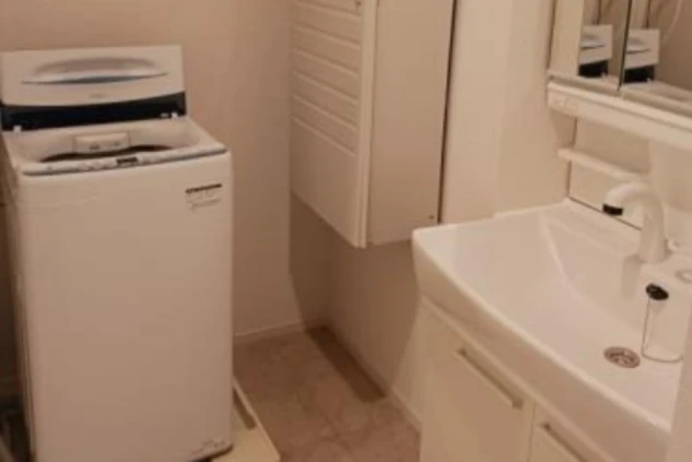 ワクトリの社員が出張で撮影した、リゾートバイトの長期寮の洗面脱衣所の画像。洗面台の隣には縦型洗濯機が設置されており、上部には収納棚も見える。リゾートバイト中の身だしなみや洗濯に便利な設備。