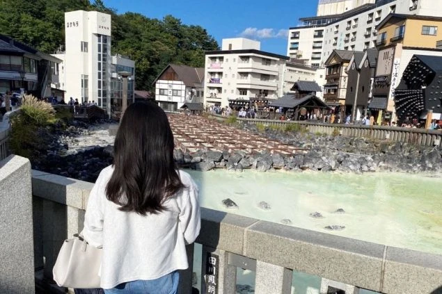 草津温泉の観光地「湯畑」の前にたたずむワクトリ女性スタッフの画像。