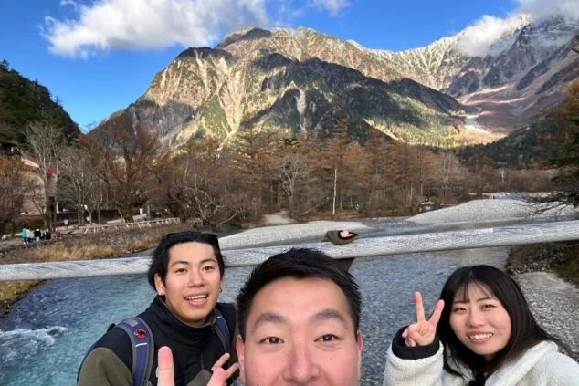 日本屈指の山岳景勝地、上高地・河童橋での記念撮影。リゾートバイトの仲間たちと、雄大な穂高連峰をバックに、最高の笑顔でピースサインをしています。