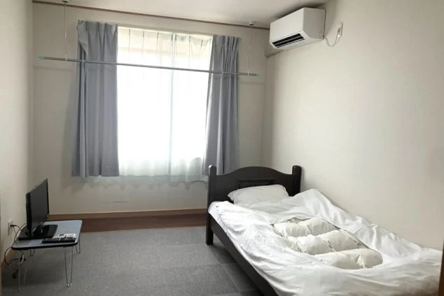 リゾートバイト用スタッフ寮の画像。ベッド、テレビ、エアコン、室内物干し竿が完備された、清潔感のあるフローリングの完全個室。