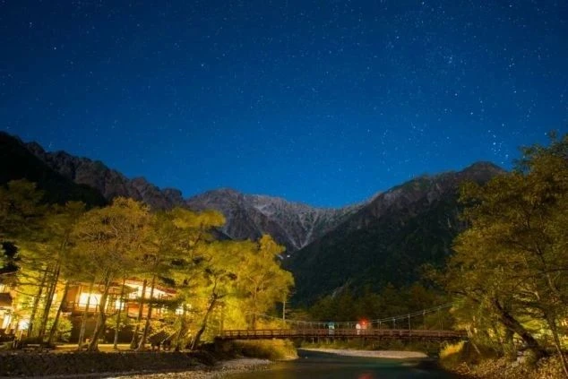 静寂に包まれた夜の上高地。ライトアップされた河童橋と背後の山々が、星が瞬く深い紺色の夜空の下で幻想的に浮かび上がっている。自然の雄大さと夜の静けさを感じる一枚。