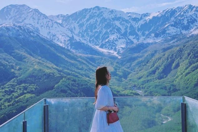 長野県 白馬岩岳マウンテンリゾートの展望台「HAKUBA MOUNTAIN HARBOR」。新緑の山々を眺める女性。リゾートバイトの休日観光。